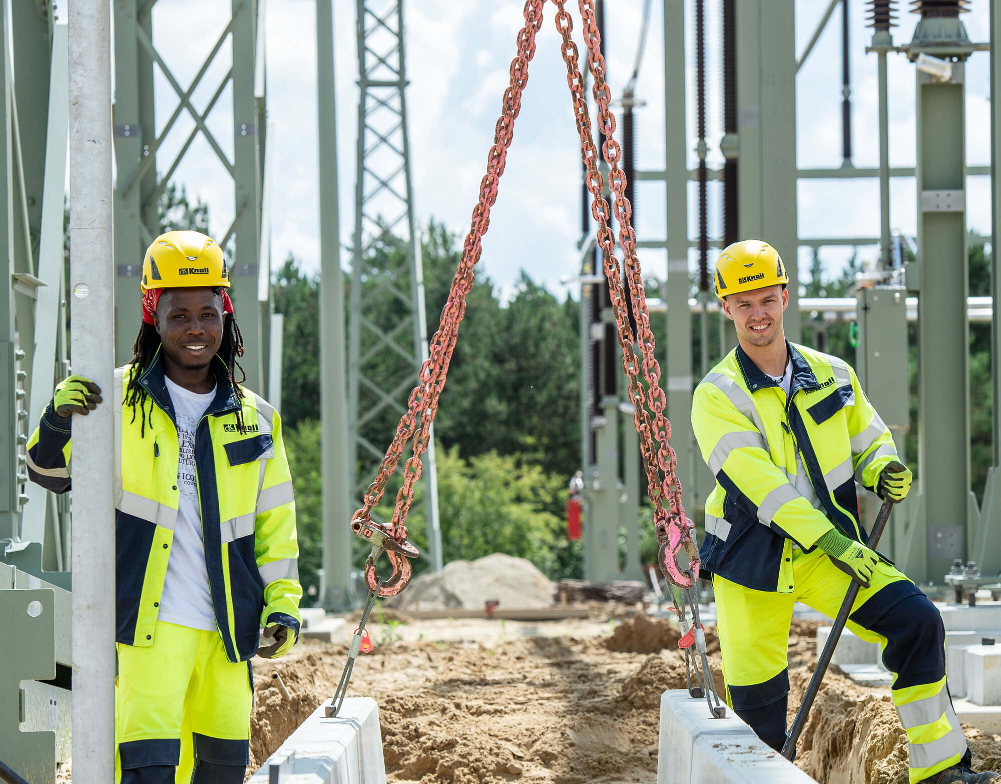 Zwei Auszubildende zum Tiefbaufacharbeiter auf einer Baustelle eines Umspannwerks mit Hebetechnik.