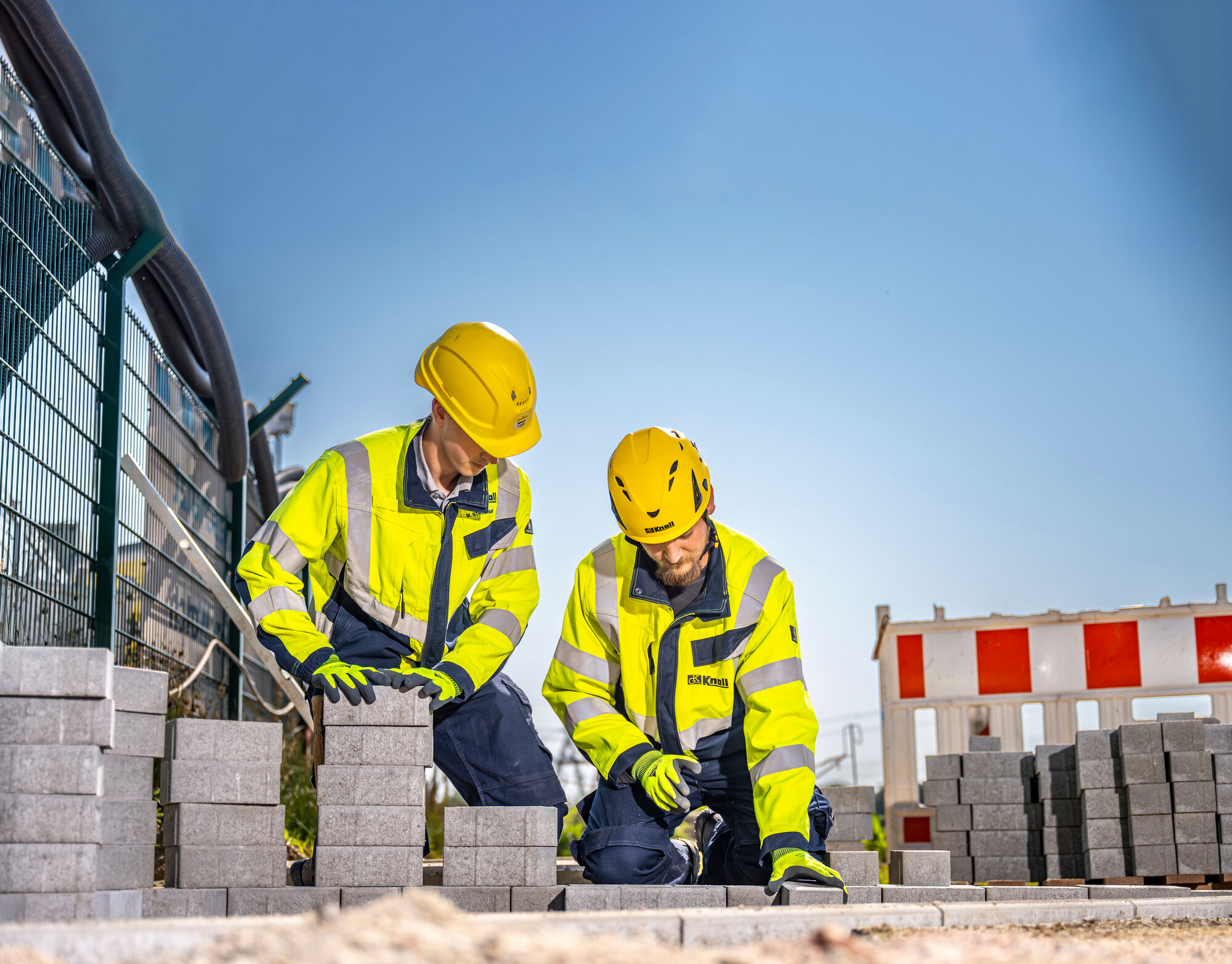 Zwei Auszubildende zum Straßenbauer setzen Pflastersteine auf einer Baustelle.