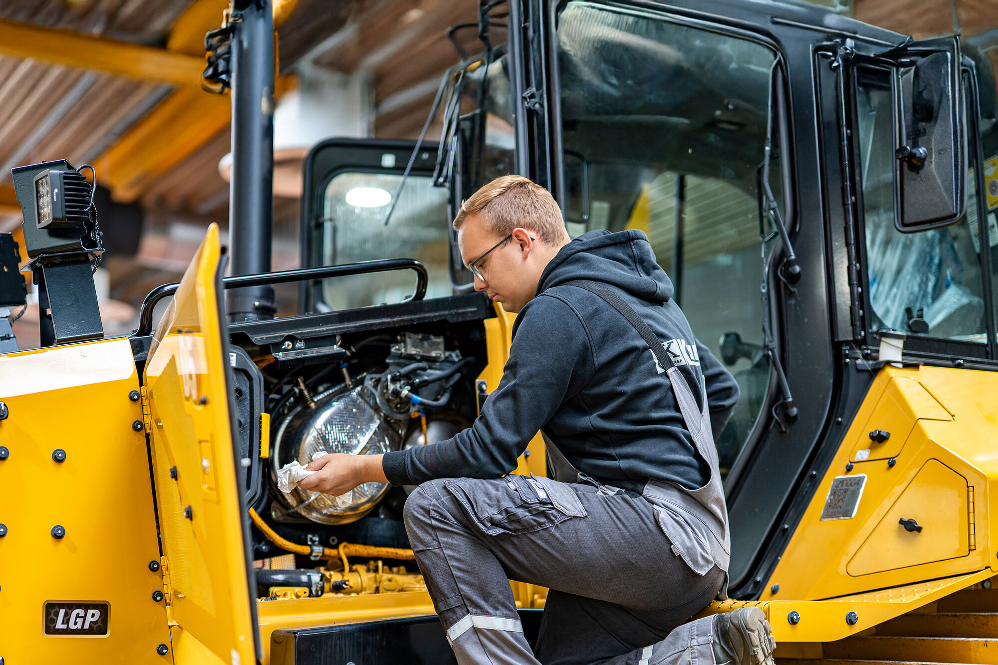 Auszubildender führt Wartungsarbeiten an einer Baumaschine in der Werkstatt durch.